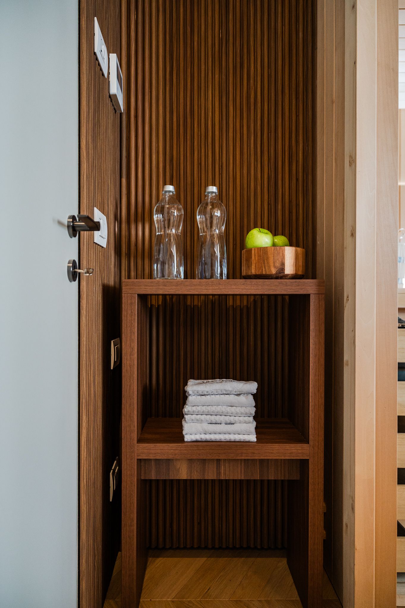 Mensola spa in noce con bottiglie d'acqua, mele verdi e asciugamani accanto alla sauna